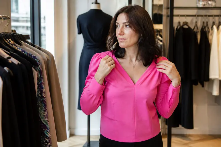 Une femme d'une trentaine d'années essaie une blouse colorée avec un décolleté en V dans une boutique parisienne, observant son reflet.