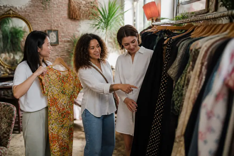 Trois amies explorent une boutique vintage à Lyon, comparant différentes robes crayon aux styles et motifs variés pour trouver leur coup de cœur.