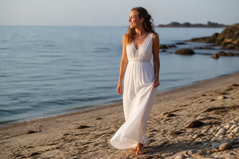 Jeune mariée choisissant une robe simple et fluide, se déplaçant avec aisance sur une plage bretonne au coucher du soleil.