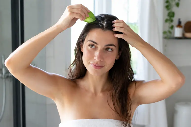 Jeune femme appliquant du gel d'aloe vera pour les cheveux sur son cuir chevelu.