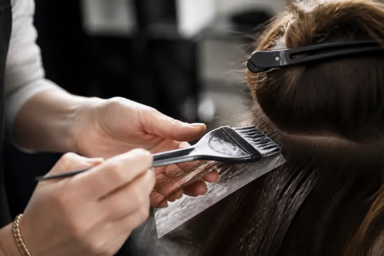 Coiffeur réalisant un balayage discret sur cheveux châtain en salon.