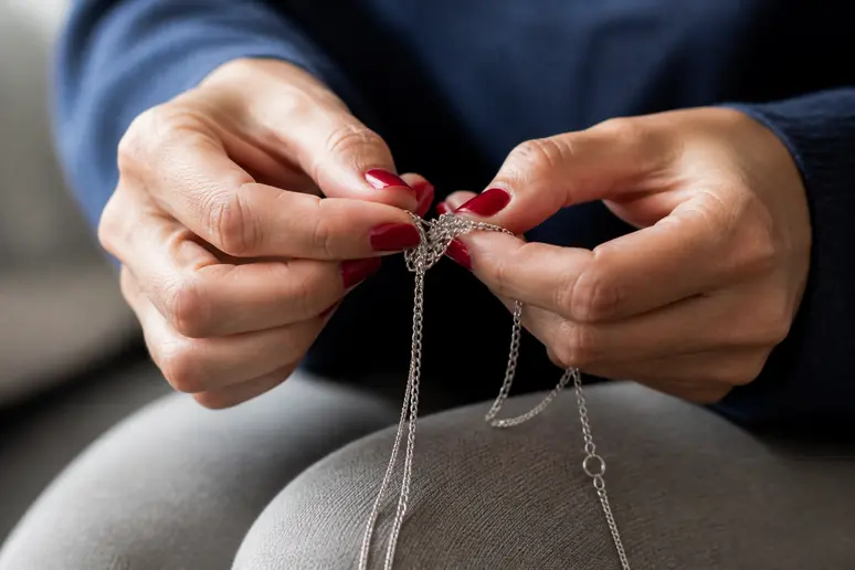 Mains soignant un collier qui s'emmêle, reflet de la signification spirituelle.