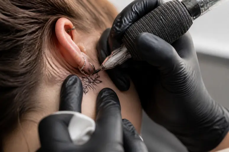 Tatouage derriere oreille signification : gros plan sur les mains d'un tatoueur créant un motif fin.