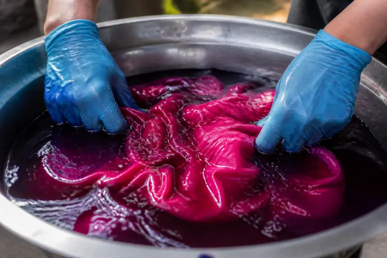 Teindre un vêtement à la main : immersion et brassage délicat du tissu dans le bain de teinture pour une couleur uniforme.