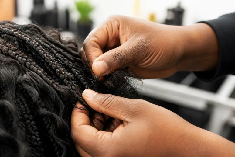 Professionnel retirant délicatement des tresses collées pour homme dans un salon.