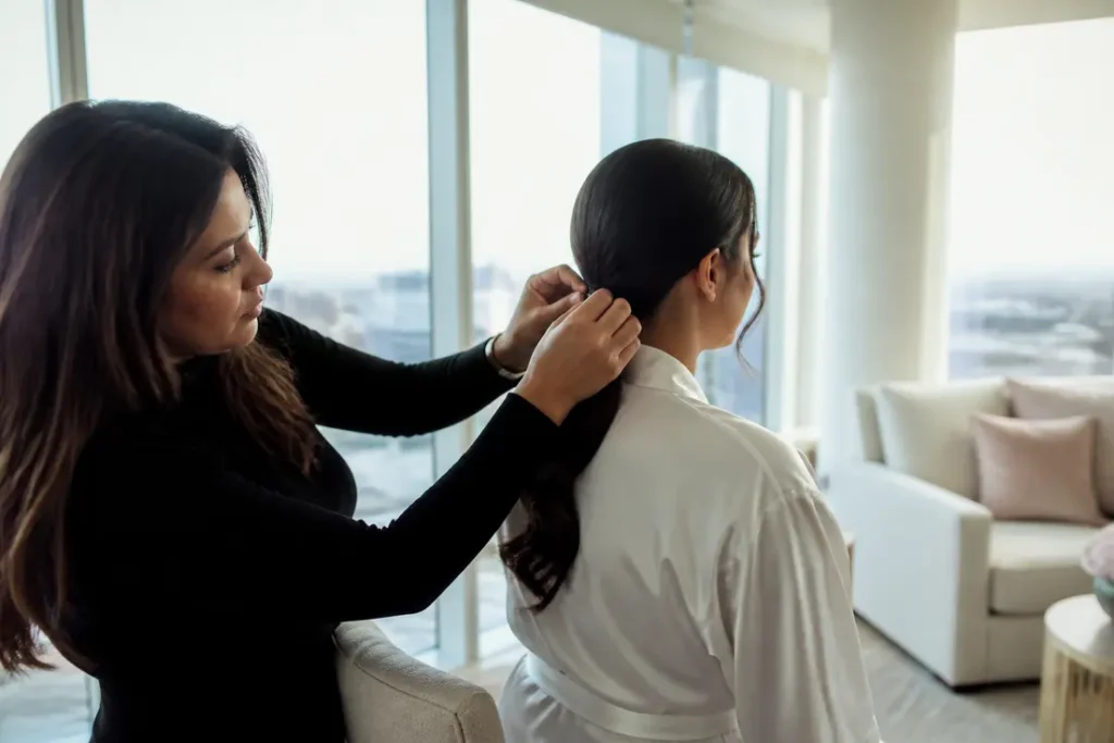 Une coiffeuse ajuste une élégante coiffure mariage queue de cheval basse sur une mariée