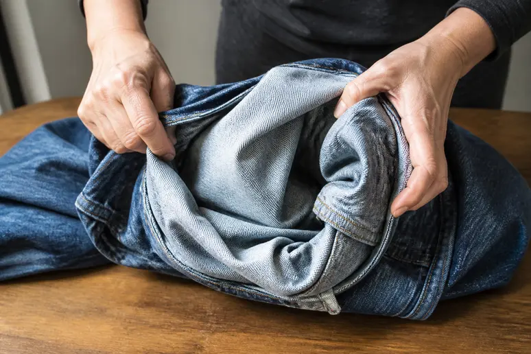 Mains retournant un jean à l'envers sur une table en bois pour le rétrécir par la chaleur