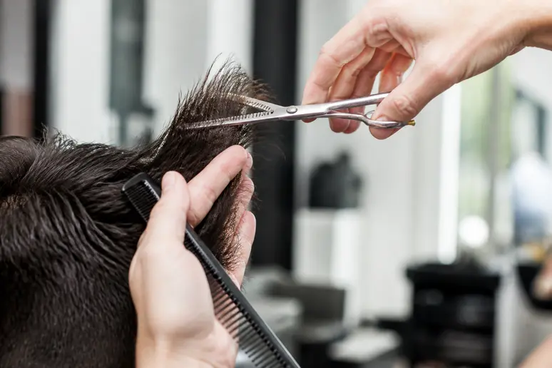 Coiffeur utilisant des ciseaux sculpteurs pour désépaissir une coupe femme cheveux épais en salon