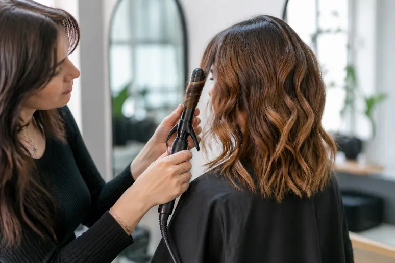 Coiffeur créant des ondulations souples pour une coupe femme visage carré.
