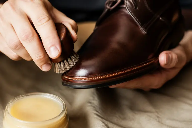 Application d'un baume nourrissant sur les coutures d'une chaussure en cuir gras avec une brosse.