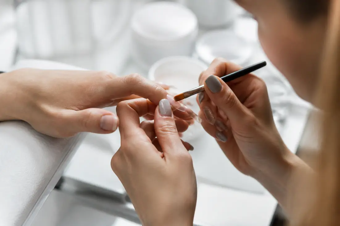 Geste précis d'une manucure en salon pour une pose américaine ongles soignée.