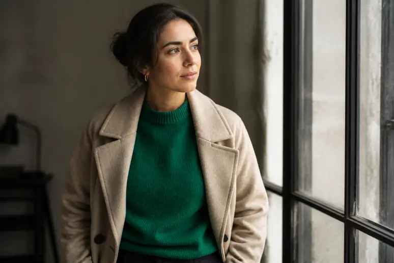silhouette portant un pull vert émeraude associé à un manteau beige neutre