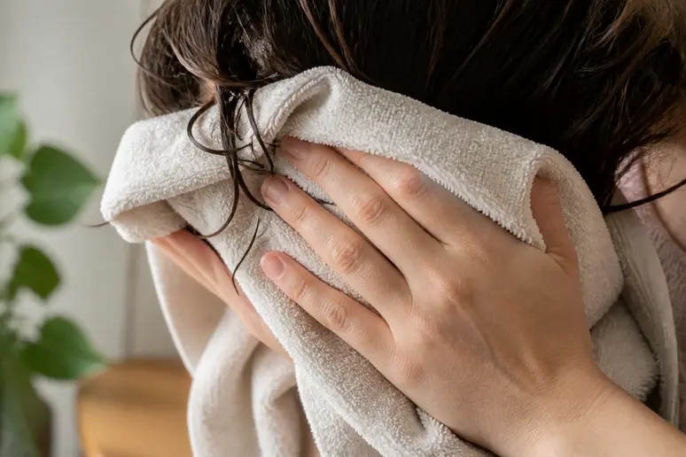 Mains essorant délicatement les cheveux humides avec une serviette en coton pour éviter la casse