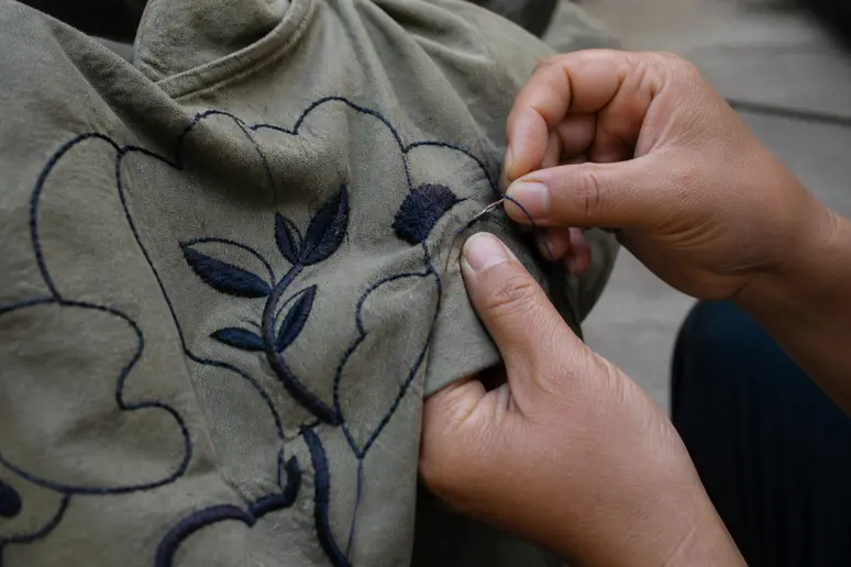 Mains cousant un motif à la main sur une veste en jean pour un look underground