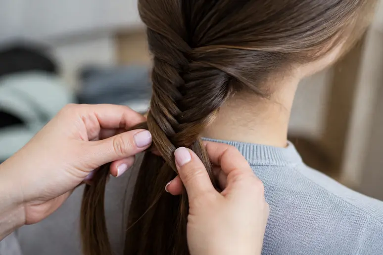 Mains réalisant une tresse épi de blé en séparant de fines mèches de cheveux