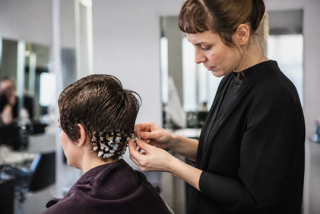 Cliente en salón de belleza recibiendo tratamiento de cabello corto permanente con rulos pequeños