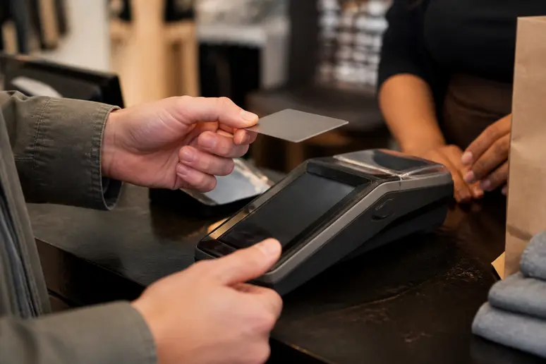 Mains d'un client présentant une carte cadeau sur un terminal de paiement en magasin