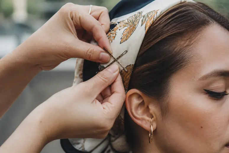 Mains fixant un foulard cheveux femme avec des épingles plates croisées près de la tempe