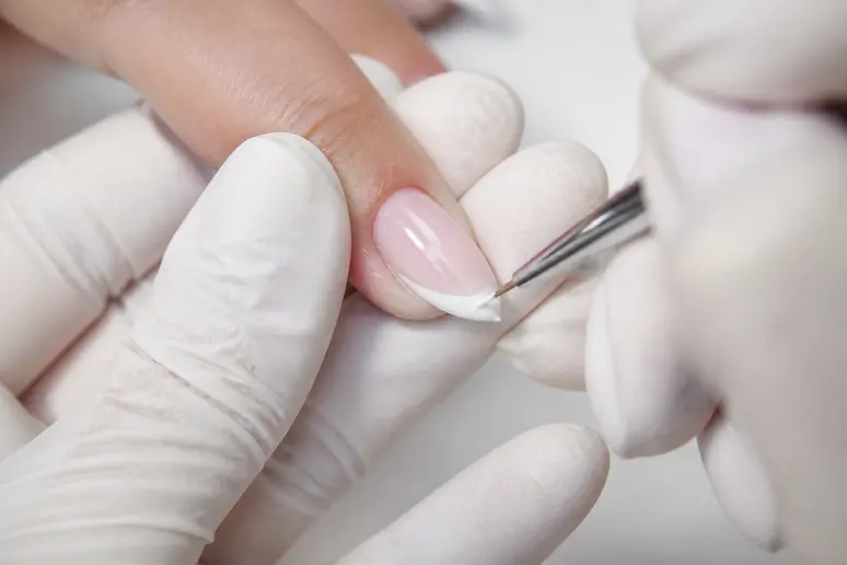 Application minutieuse d'une french manucure à l'aide d'un pinceau fin sur le bord de l'ongle