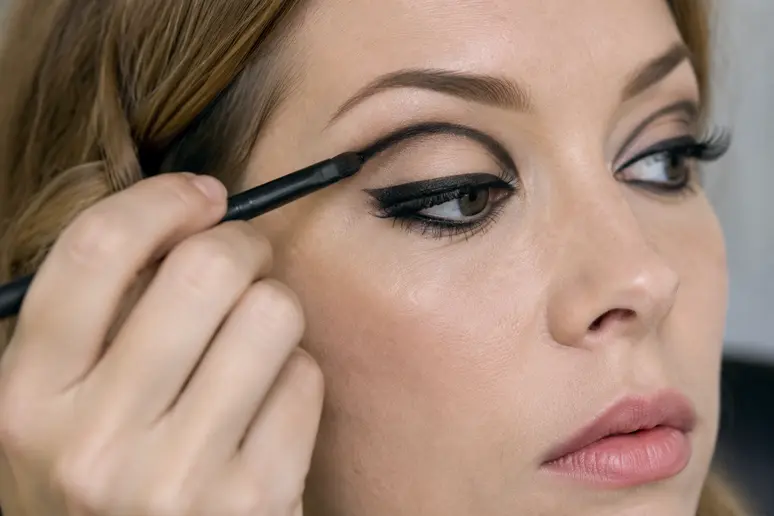 Application d'un eyeliner graphique et tracé du pli de paupière pour le maquillage année 60.