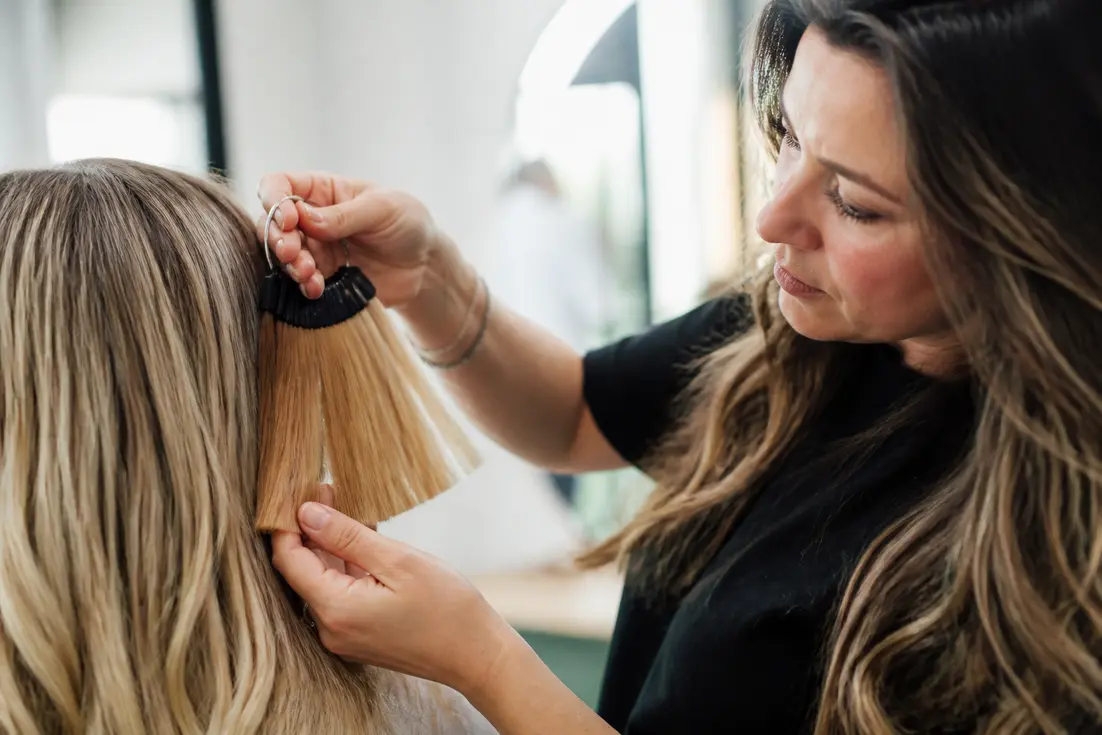 Un coiffeur analyse des mèches avec un nuancier couleurs cheveux en salon pour éviter les reflets cuivrés.
