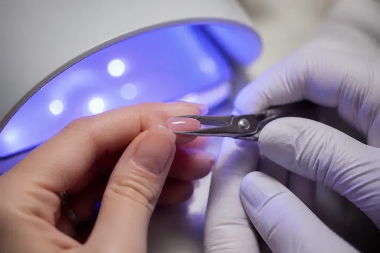 Pince métallique exerçant une pression latérale mesurée sur une extension d'ongle en gel.