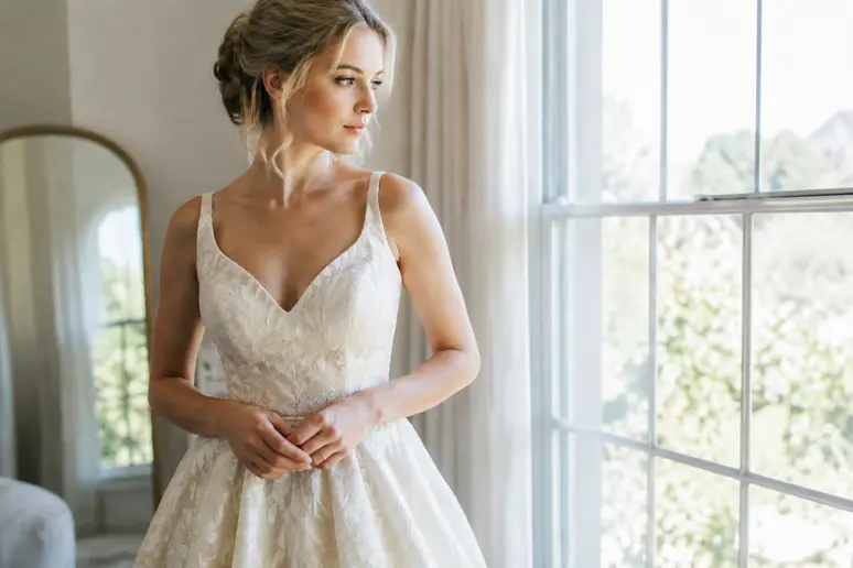 Essayage d'une robe de mariée ivoire près d'une fenêtre pour observer l'effet sur une peau claire