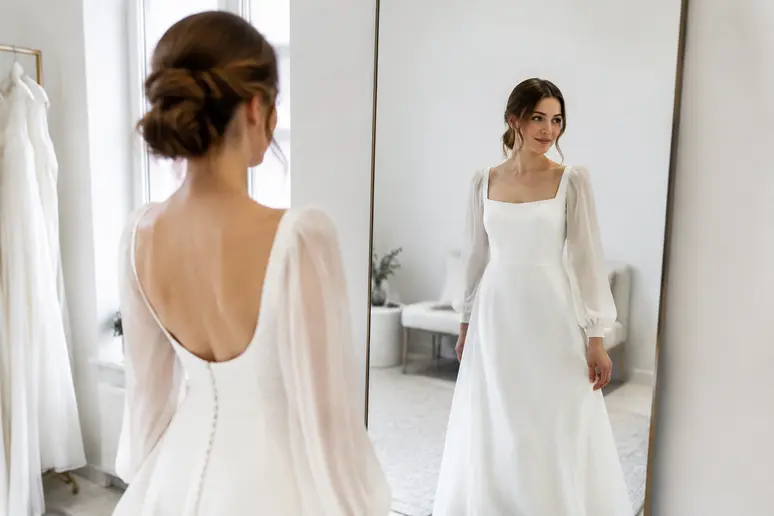 Future mariée essayant une robe de mariée manches longues fluide et souple en cabine