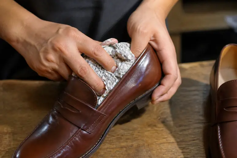 Bourrage de papier journal dans des chaussures en cuir pour modeler et assouplir la matière.
