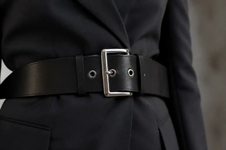 Ceinture large en cuir marquant la taille sur un blazer sombre.