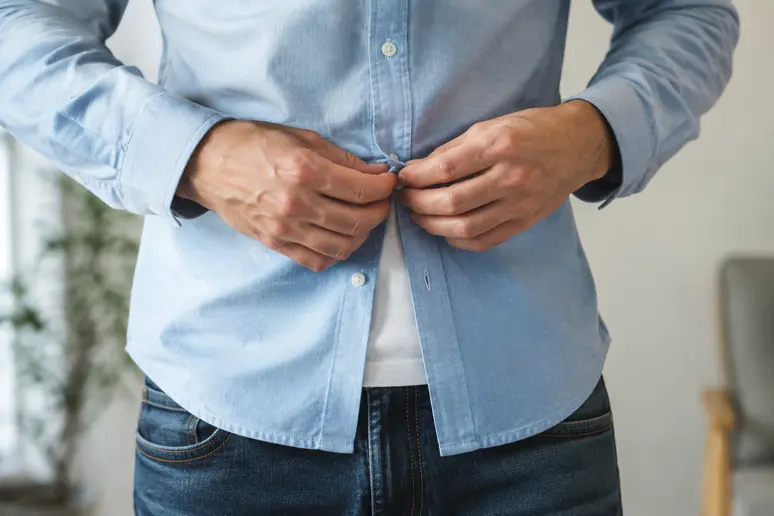 Homme boutonnant une chemise bleue sur un jean pour composer sa tenue casual chic