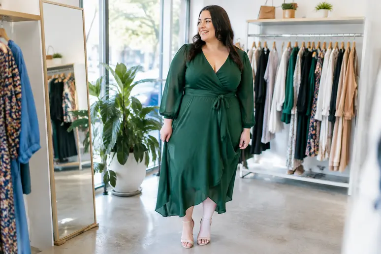 Femme essayant une robe portefeuille élégante pour un mariage en grande taille dans une boutique lumineuse.